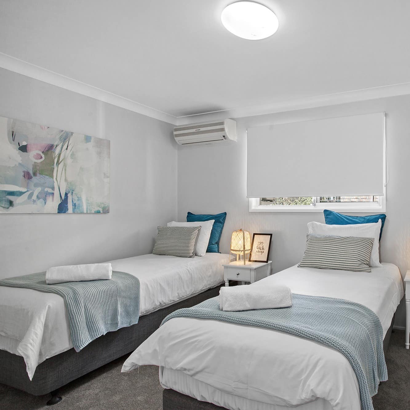 Bedroom with grey carpet, white walls, two twin beds, blue and white bedding, and abstract art.