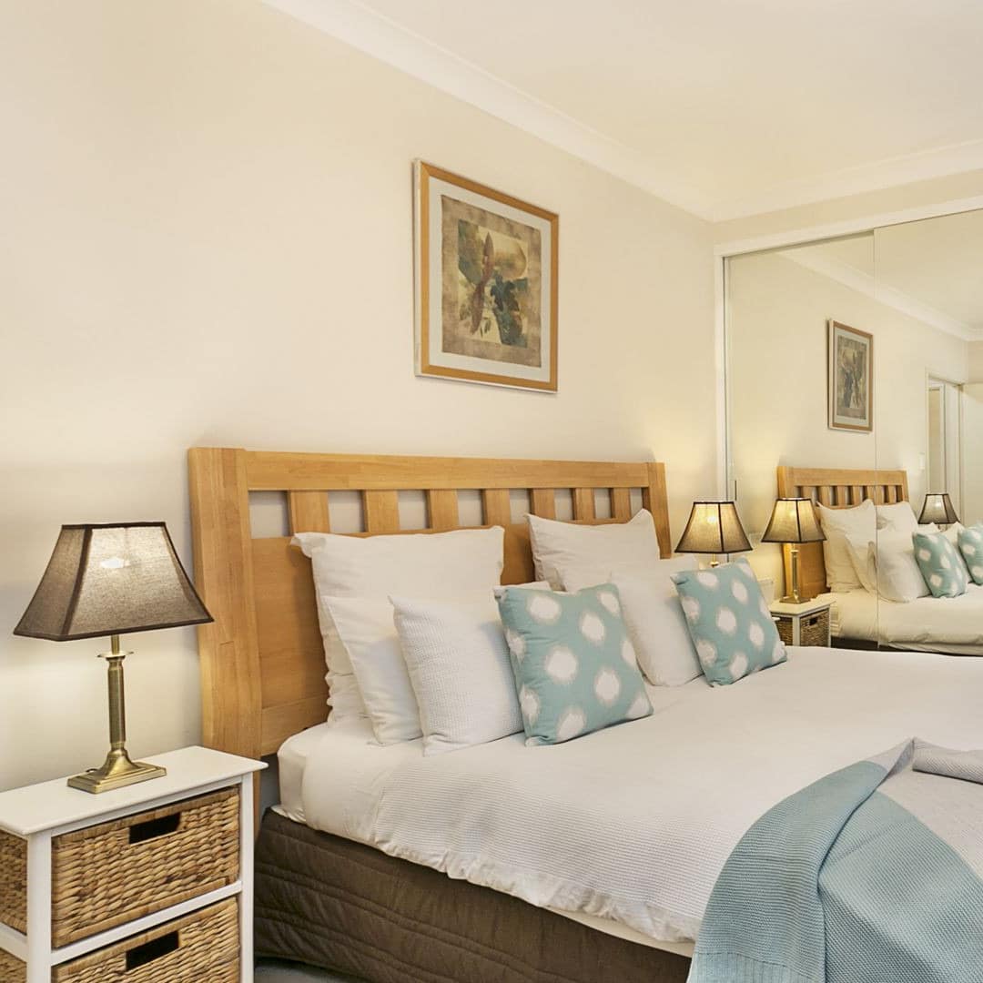 Bedroom with grey carpet, white walls, a wood-framed king size bed and white and light blue bedding.