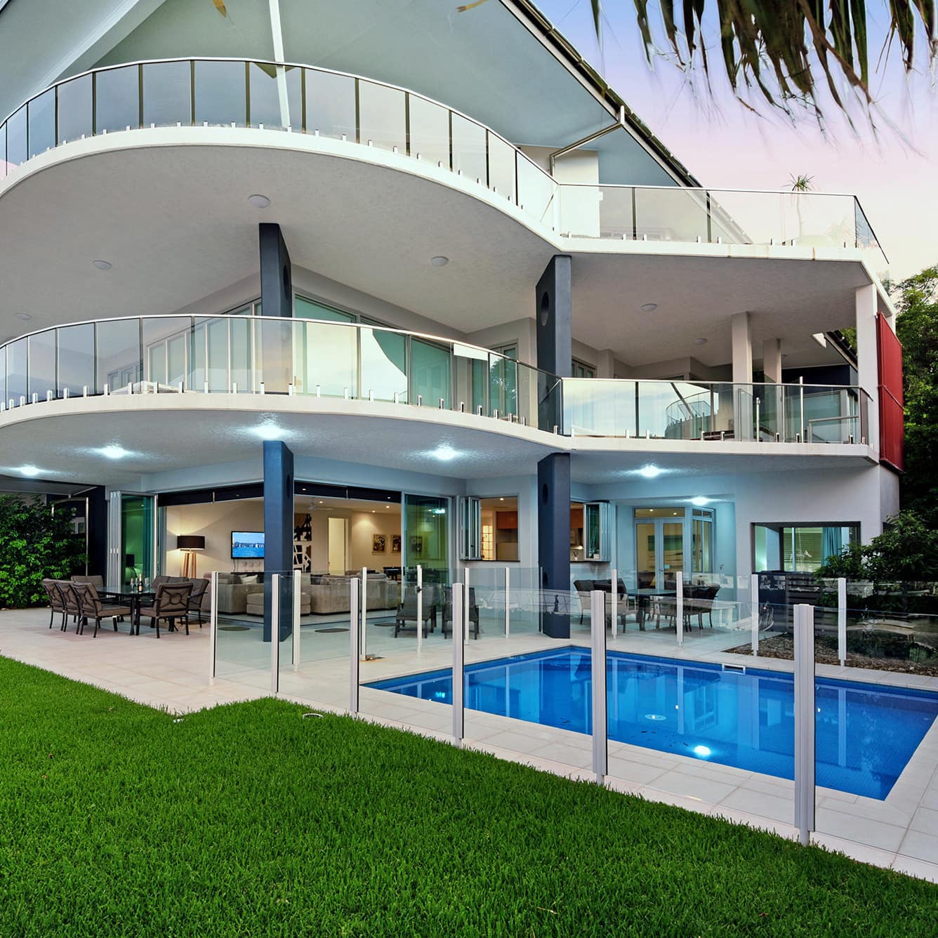 Modern two-story home with wrap-around balconies on each level, a private pool, beige tile patio space, manicured lawn.