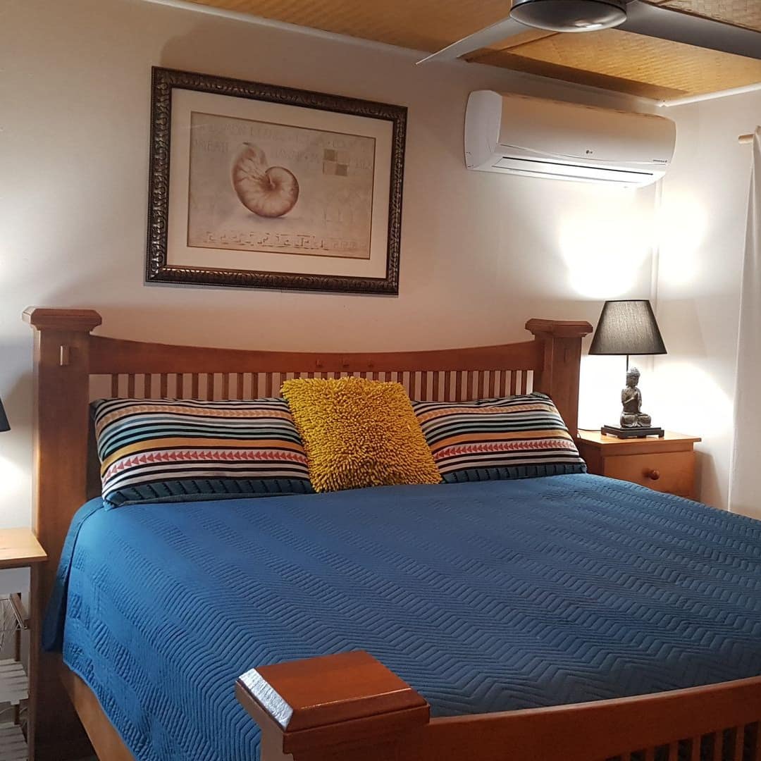 Bedroom with wood-framed king size bed, blue bedding and colorful pillows, tall windows with white curtains.