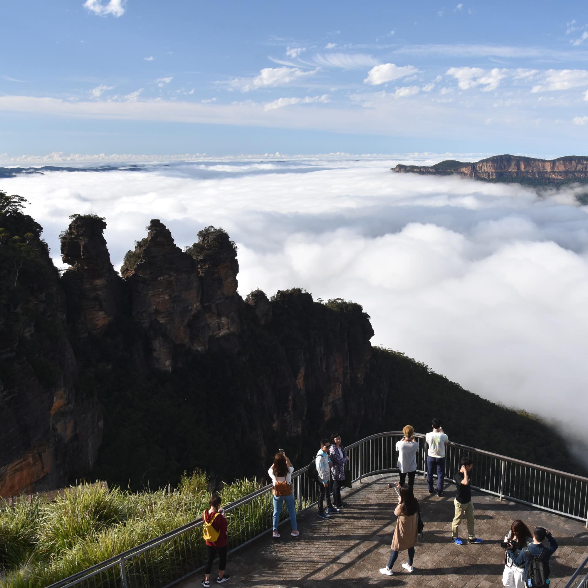 People at Echo Point take photos of Three Sisters and enjoy the mist in the valley of the Blue Mountains