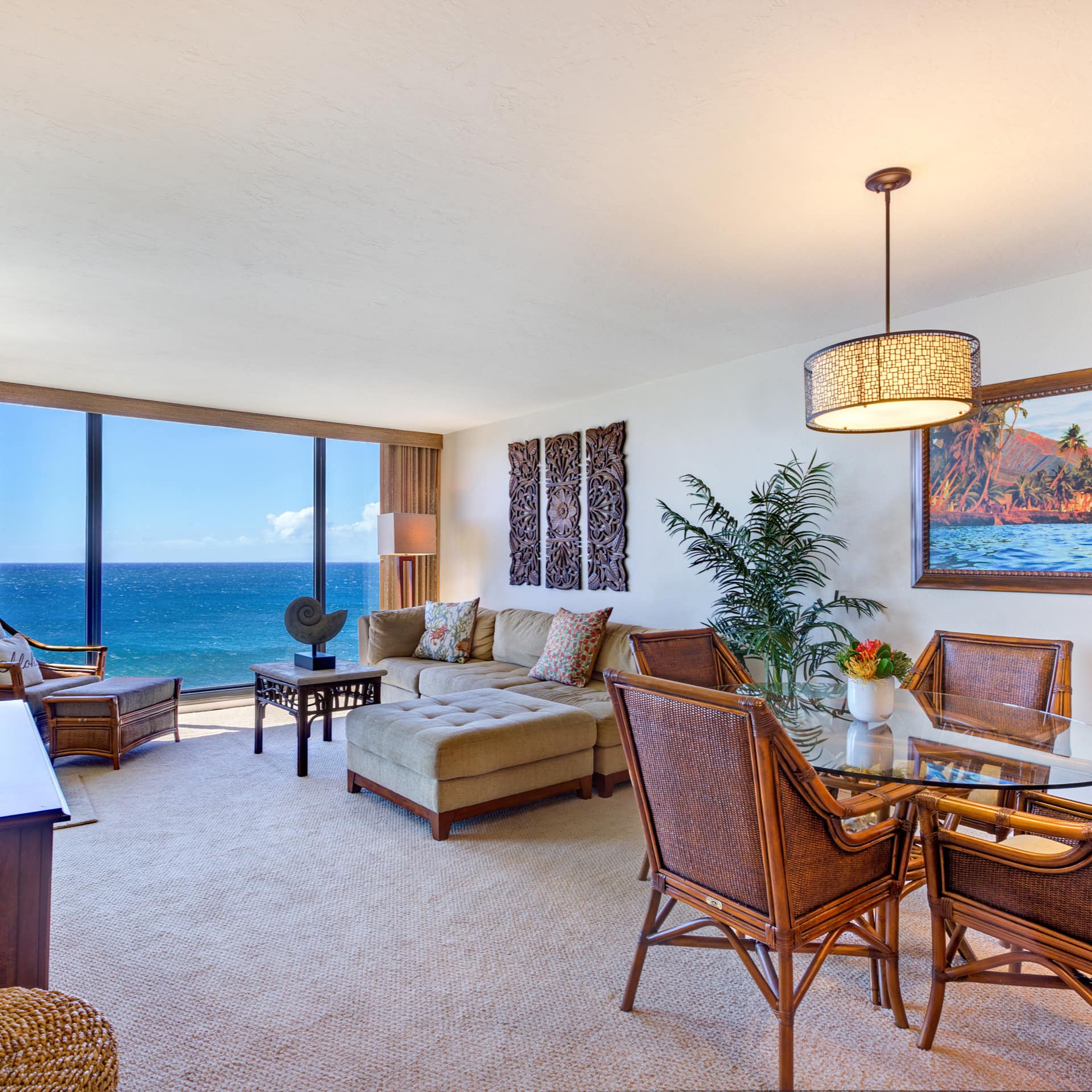 Open living and dining room with bamboo dining set, beige sectional, and floor to ceiling windows with ocean views.