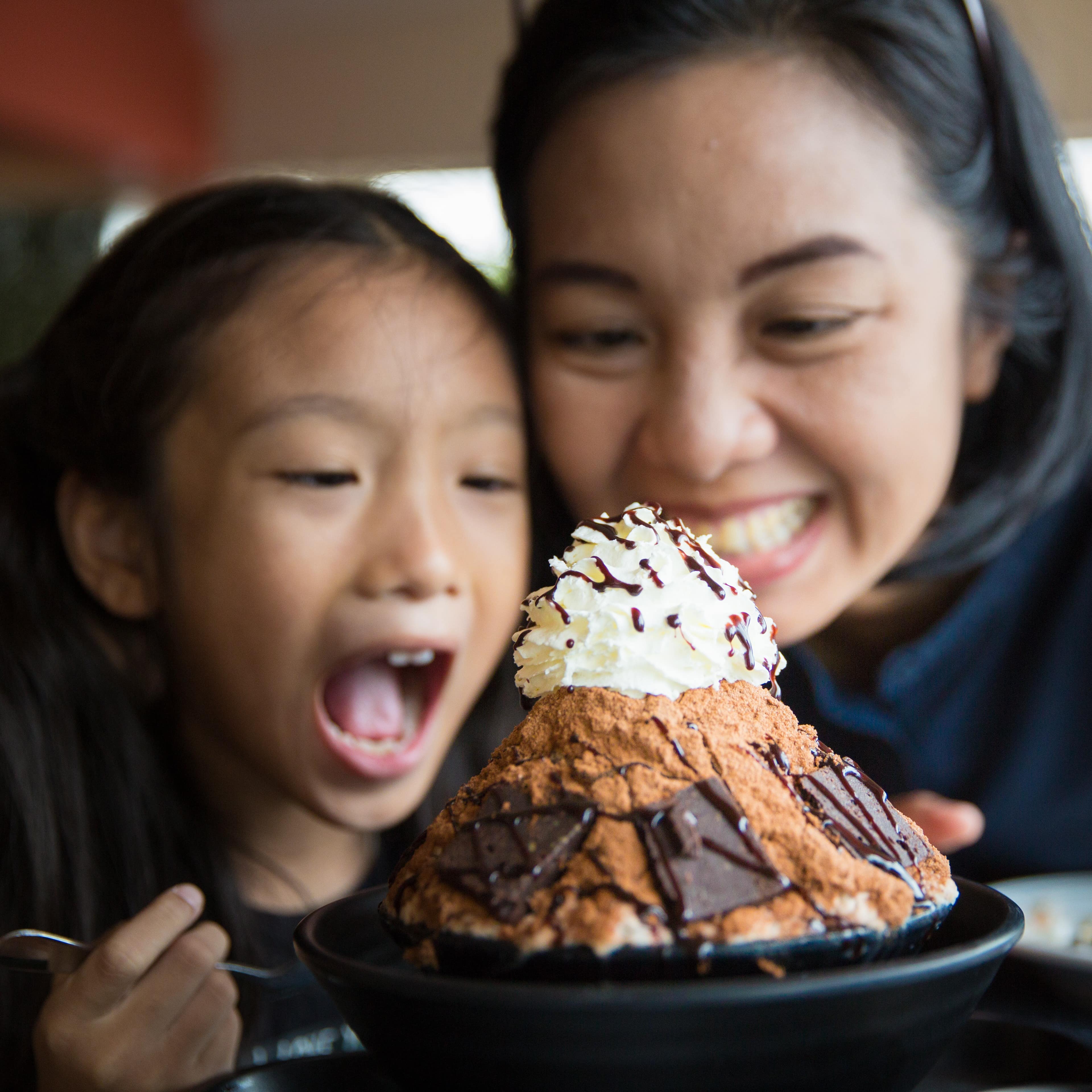 Mother and daughter happily enjoy eating an ice cream dessert