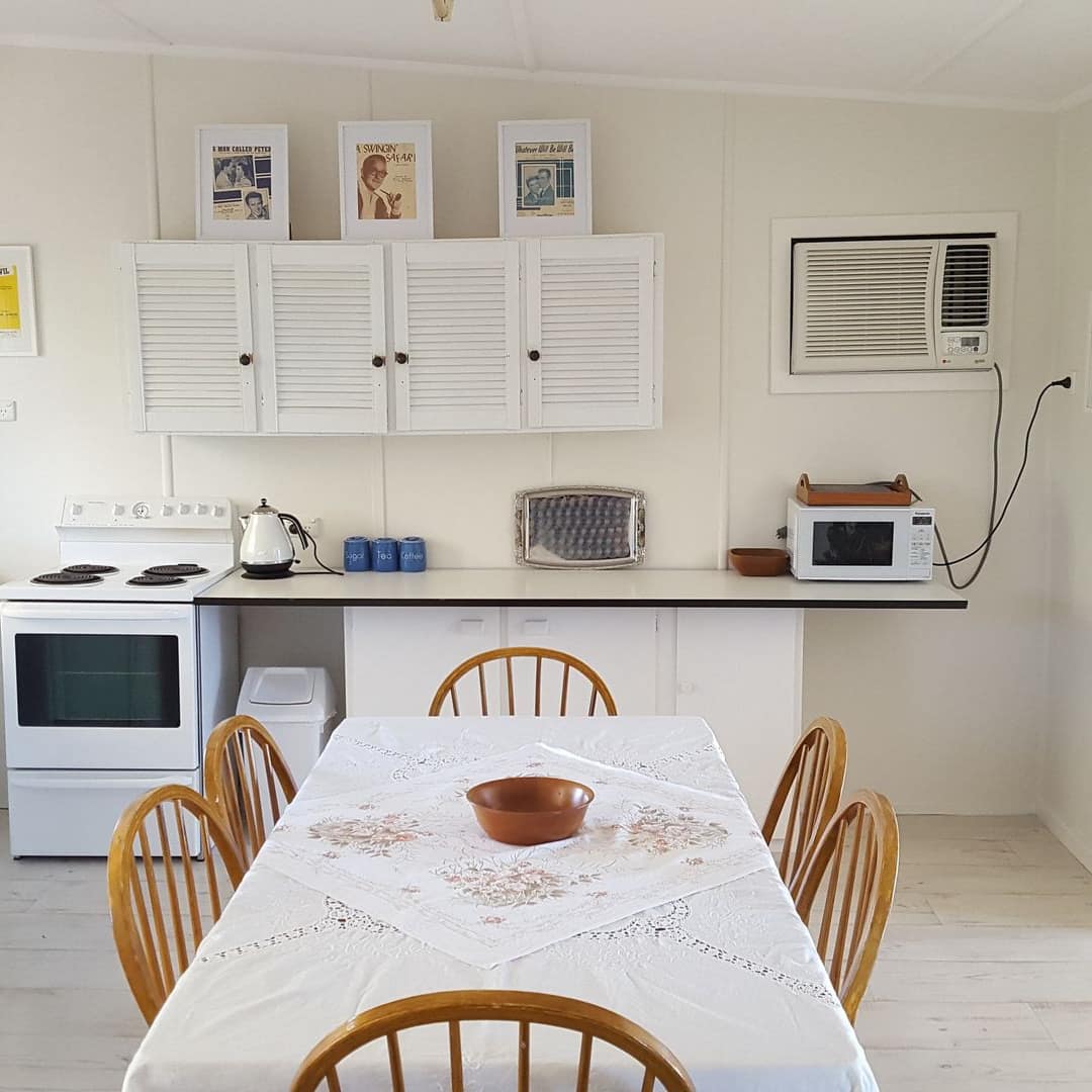 Bright open kitchen, wooden dining set with white table cloth, white cabinets and countertops, vintage art.