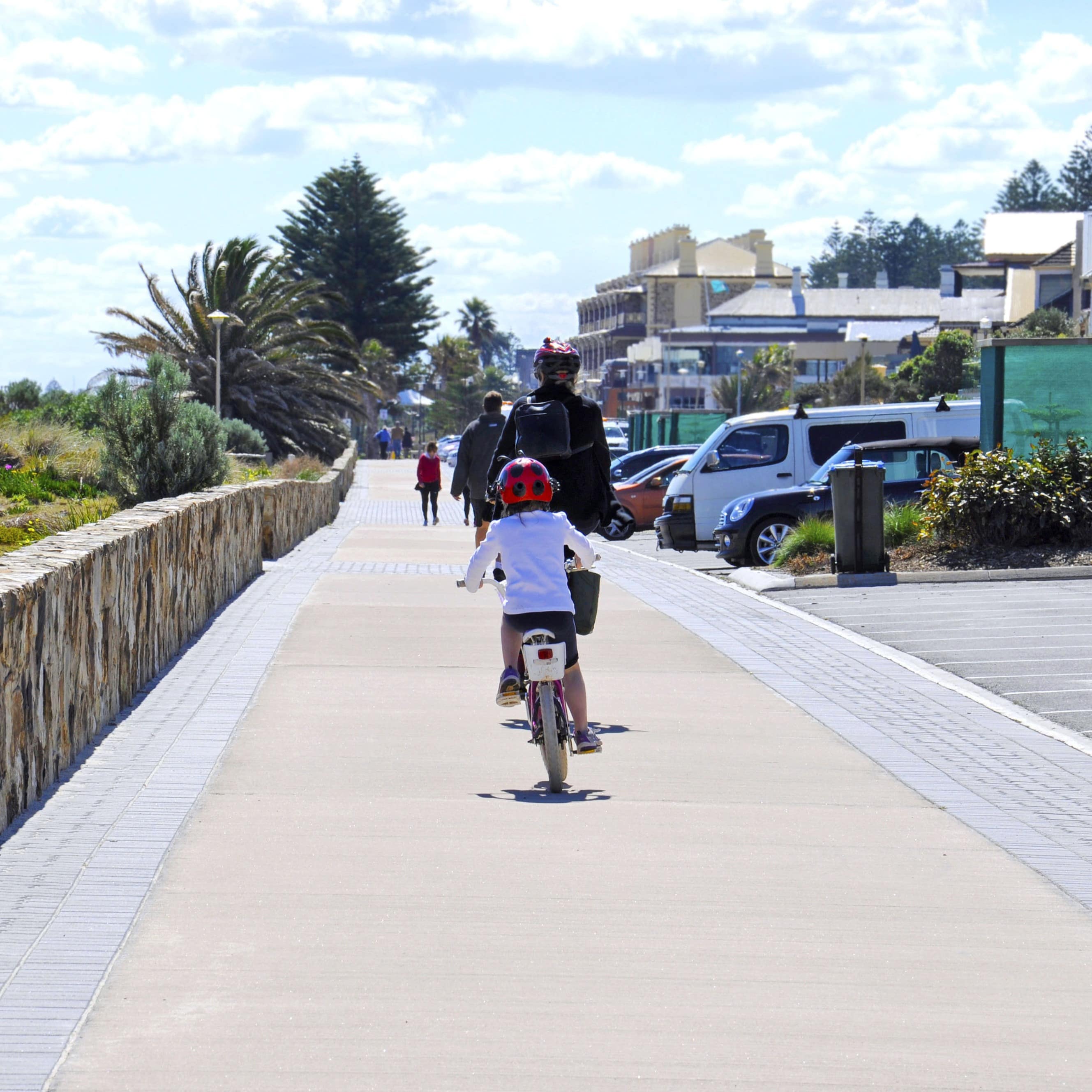 Rear view of mother and daughter riding bicycles on boardwalk along the Esplanade walkway