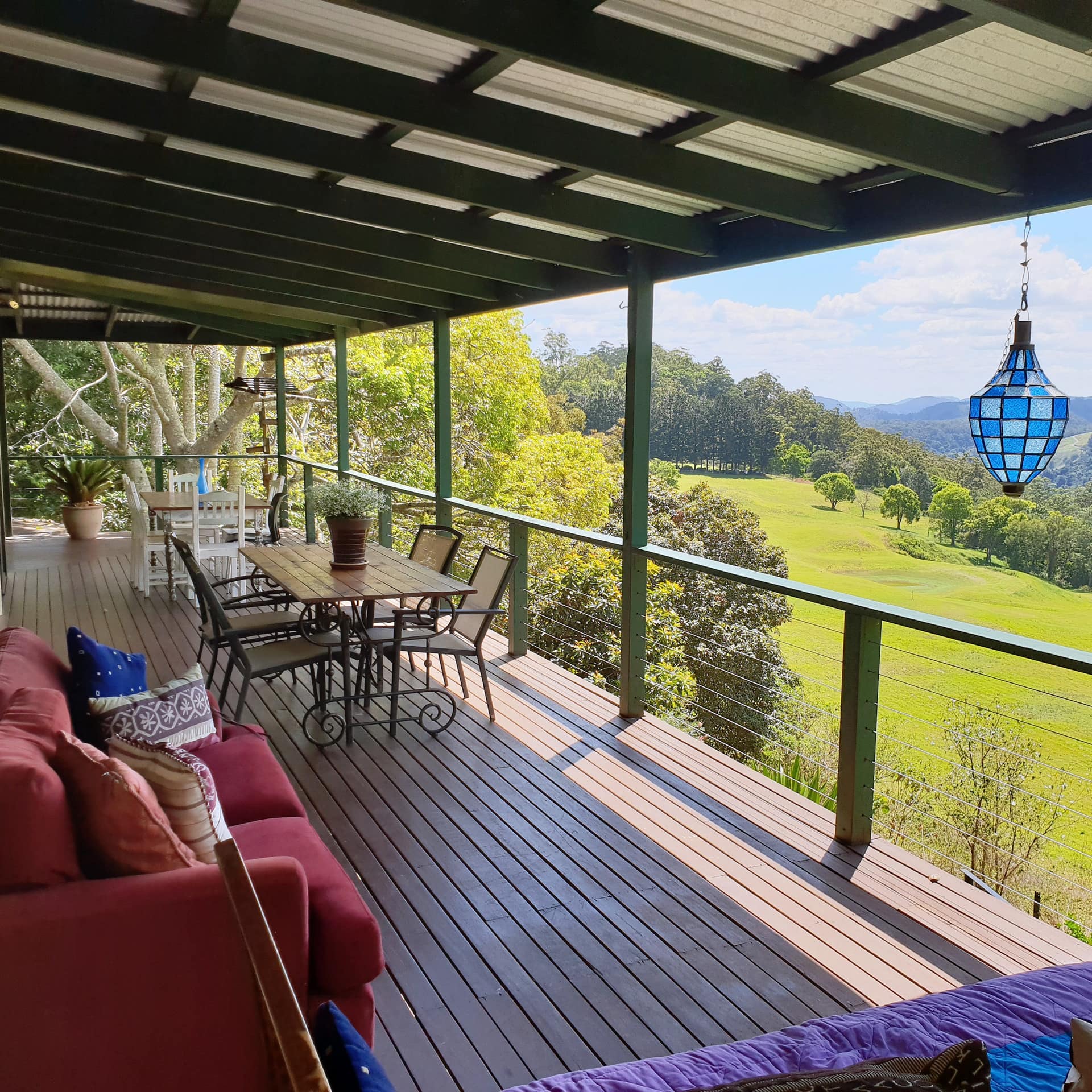 Covered verandah with wood floors, wood dining set, red sofa, and panoramic views of rambling hills and trees.