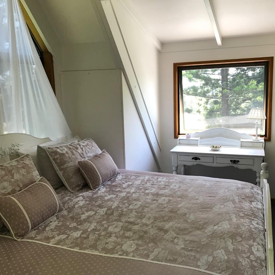 Bedroom with white walls, a king size bed, tan and white floral bedding, sheer canopy over the bed, a vintage white vanity.