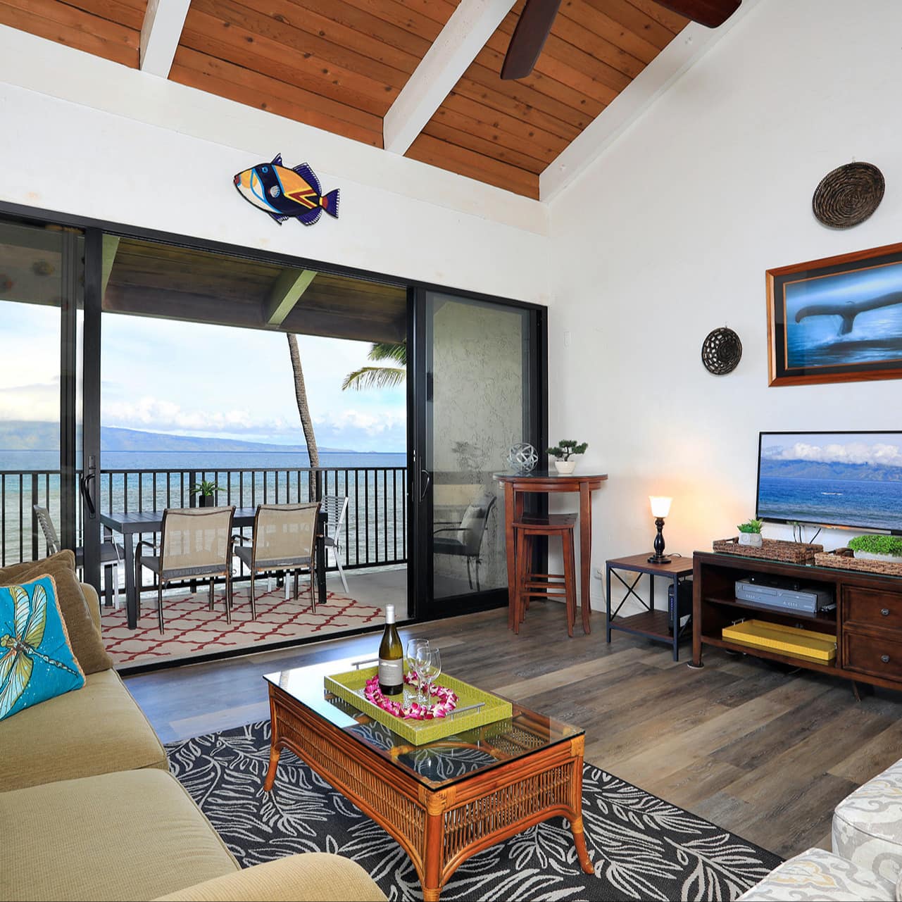 Open living room with green sofa, wooden coffee table, flatscreen TV and an attached balcony with ocean views.