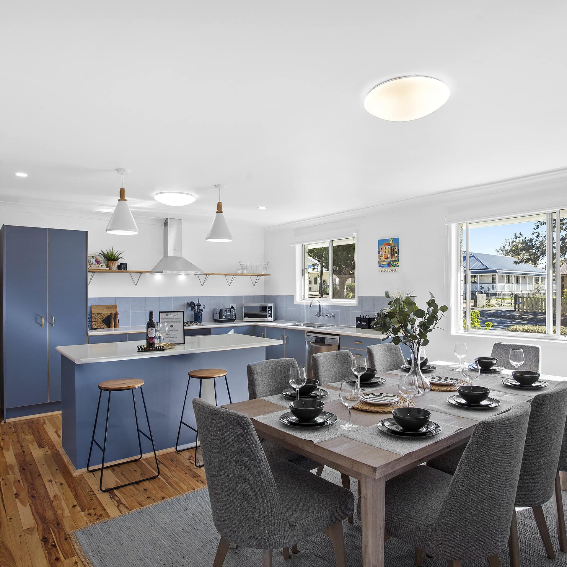 Open modern kitchen with hardwood floors, wooden dining table, blue cabinets, and kitchen island with bar stools.