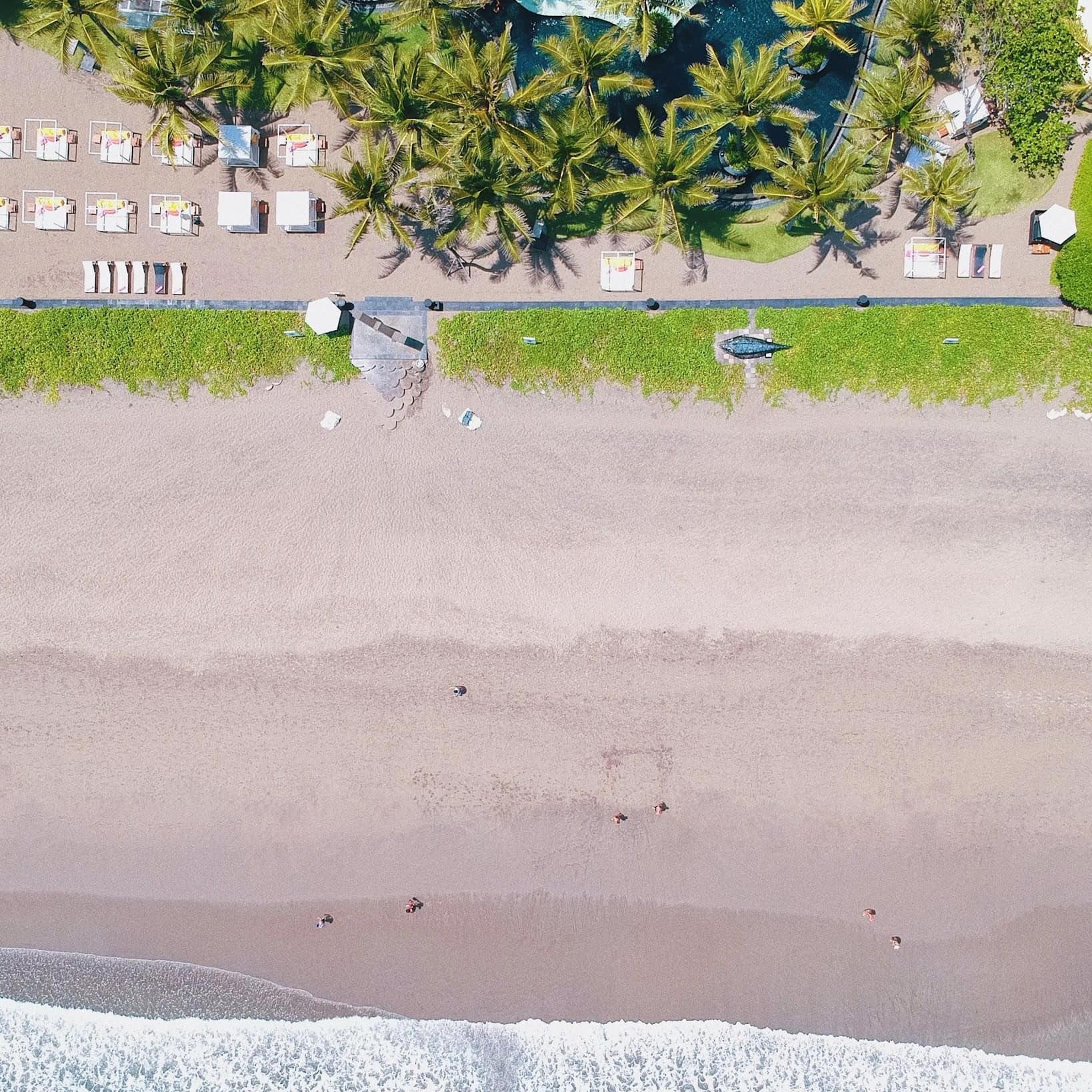 Aerial view of a beachfront villa and pool surrounded by palms and lounge areas and the beach with the Indian Ocean rushing onto the shore