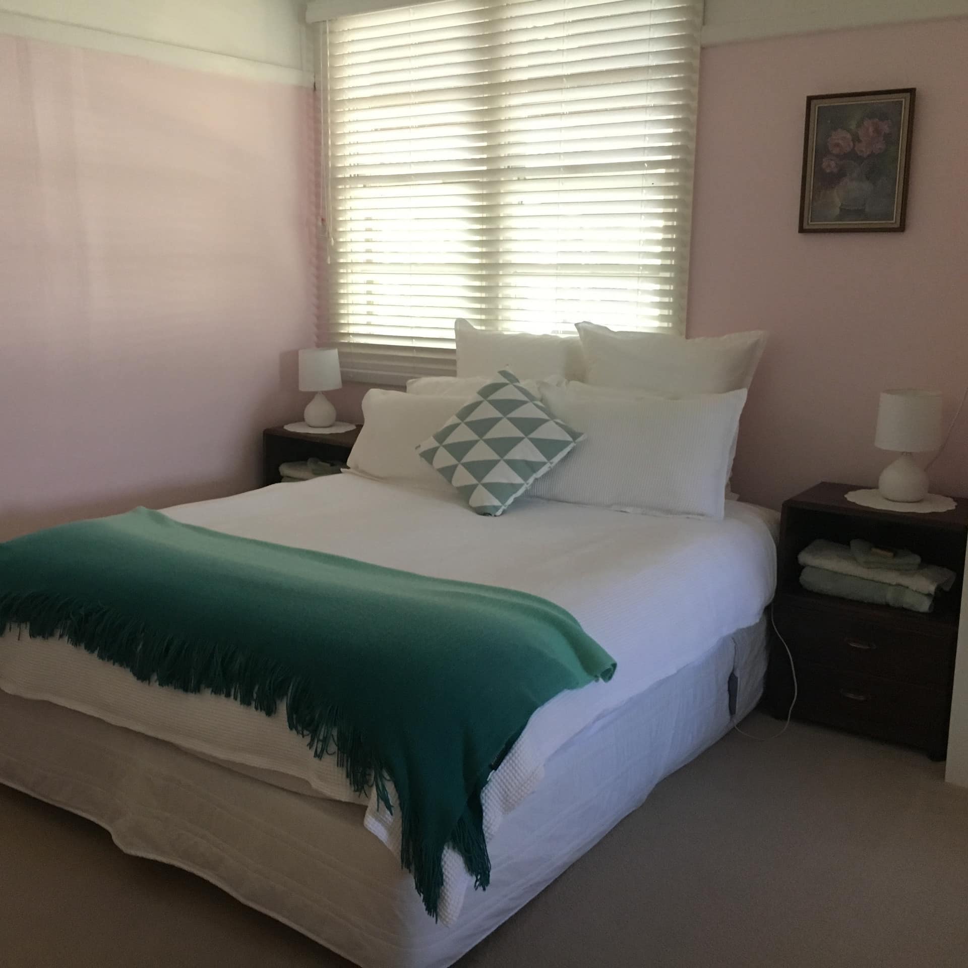 Light pink bedroom with beige carpet, a queen size bed with white linen and a green blanket.
