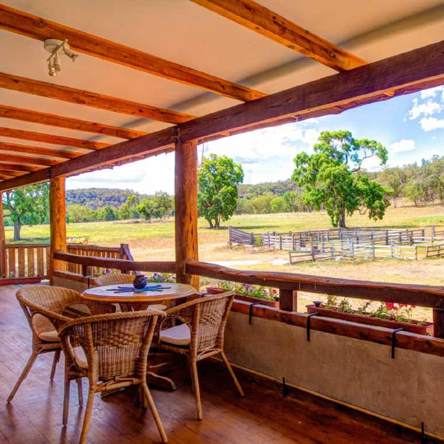 Covered wood veranda with exposed beams, wicker table and chairs, overlooking rambling fields and horse corral.