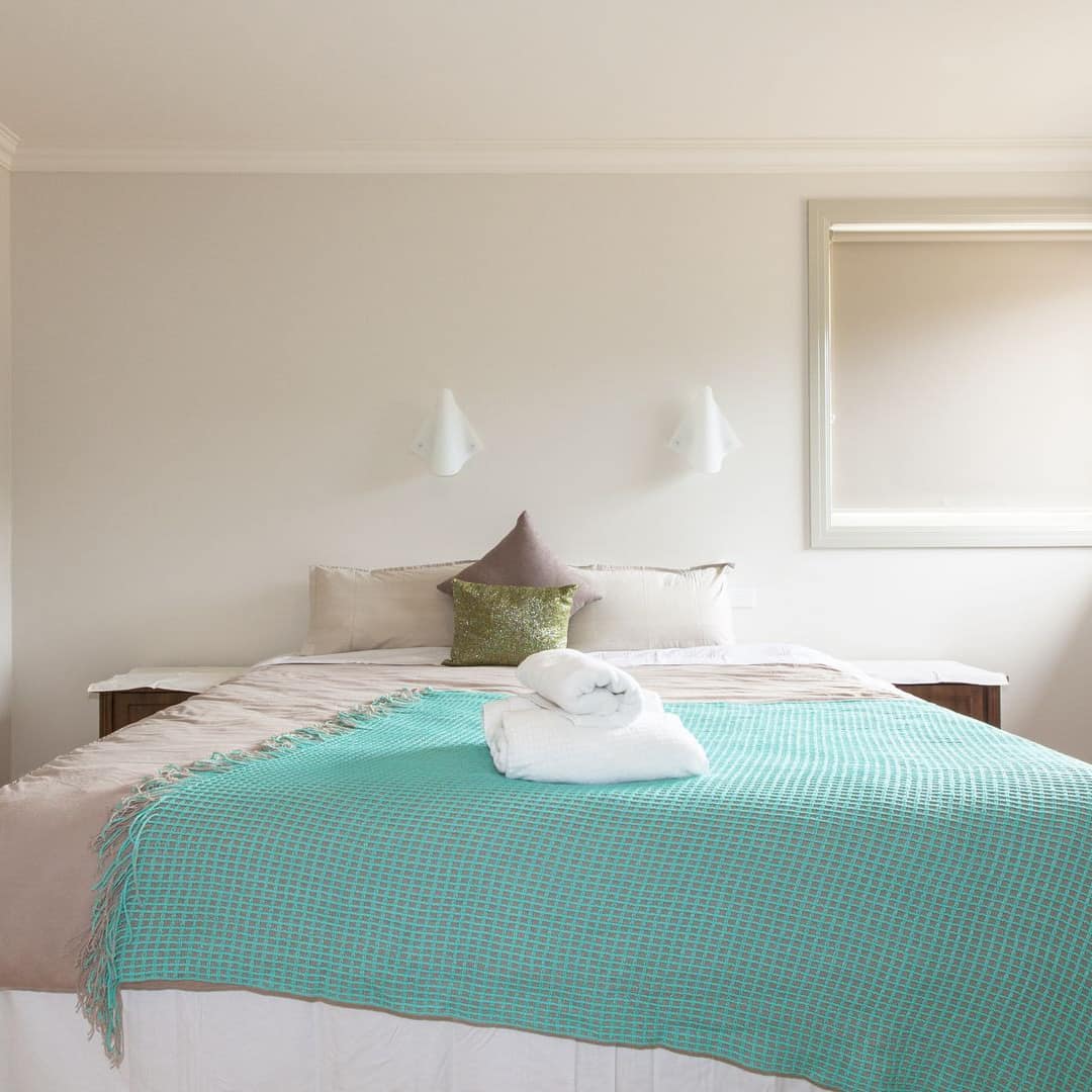 Modern bedroom with hardwood floors, white walls, queen size bed with grey and white bedding and teal blanket.