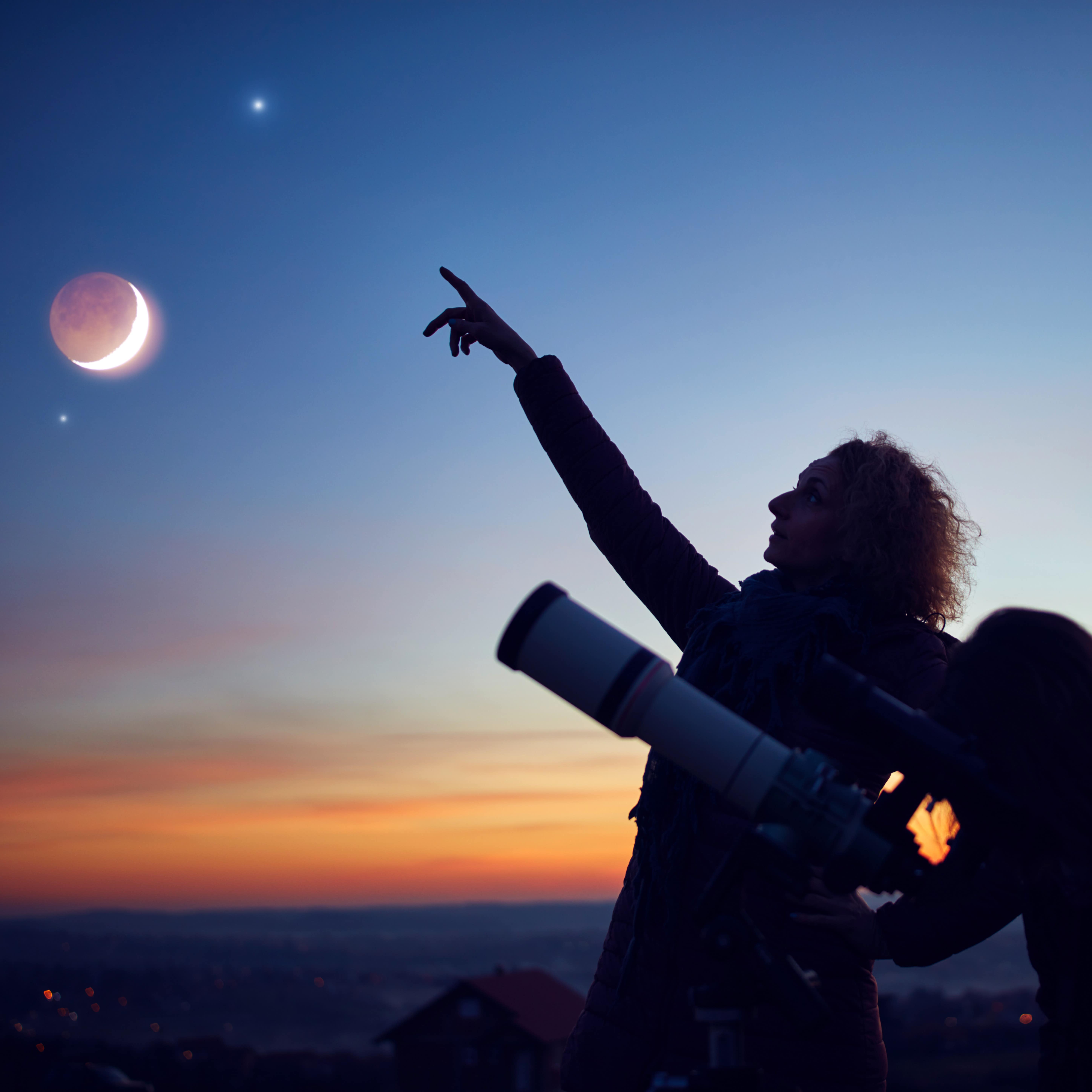 Mother and daughter observing stars, planets, Moon and night sky with an astronomical telescope